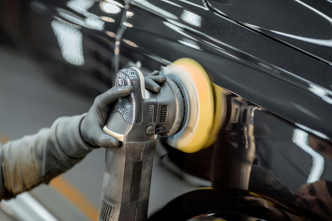 auto detailer buffing out paint scratch with powered buffer